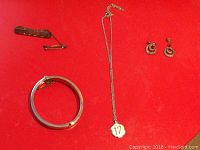 Full lot overview showing bracelet, necklace with pendant, golf pin, and earrings on red background.