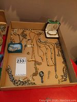 Top view of assorted costume jewellery including necklaces, bracelets, key pendants, and copper magnetic bracelets in a box.