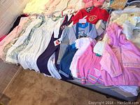 Wide view of assorted children's clothing laid out, including dresses and jackets in soft pastel colors and floral patterns.