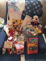 Full lot contents showing Mickey plush, books, socks, poster, small toys, collectible tin, and other items on a blue chair.