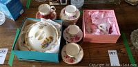 Photo showing the Royal Doulton Bunnykins warming dish in original blue box along with several teacups and saucers, including boxed swan teacup set and floral-patterned Royal Albert cups and saucers.