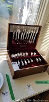 Full view of the open wooden case with all flatware pieces neatly arranged and inserted into slots.