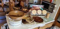 Overview of wooden bowls, serving dishes, plastic divided plates, and boxed canister set on table with other kitchen items