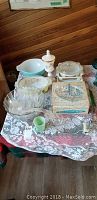 Table display of vintage Pyrex casserole dishes in pastel blue and white, glass punch set, milk glass candy dish, covered casserole, snack sets in original box, and small glass cups.