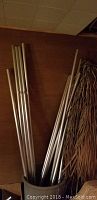 Silver metal rods and bases grouped together in a container against a wood-paneled wall.
