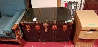 Front view of vintage steamer trunk showing black metal panels, three latches, central lock, and metal rivets.