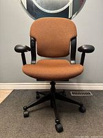 Front view of Equa chair showing rust fabric, black arms, five-star base