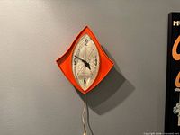Front view of orange diamond-shaped wall clock showing dial and numerals