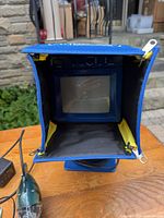 Monitor in protective hood, camera, cable reel, AC adapter visible on table
