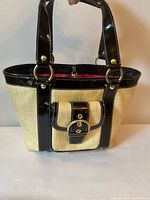 Front view of Coach straw tote showing black patent trim, buckle pocket, handles