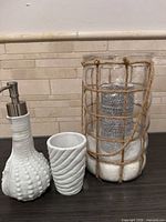 all four items grouped: ceramic soap dispenser, tumbler, rope-wrapped glass hurricane with candle