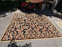 Full view of rectangular wool area rug on driveway showing floral oriental pattern and border