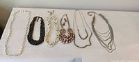 All six necklaces and earrings laid out side by side on white surface