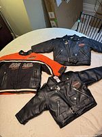 All three Harley-Davidson children’s jackets laid out showing fronts, belts, zippers, logos and color details