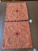 Two red and gold paisley wool pillow covers laid flat showing full pattern