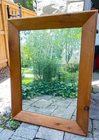 Full view of rectangular wall mirror leaning outdoors showing wood frame and reflective glass