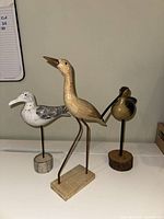 Front view of three carved wood bird figurines on stands