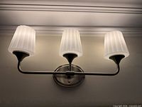 Wall sconce illuminated showing three frosted glass shades and brushed nickel finish
