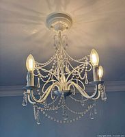 Chandelier lit showing white frame, five bulbs, crystal beads and drops