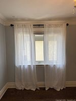 Full view of white sheer panels hanging on black rod over window