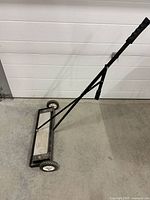 Front angled view showing entire magnetic sweeper with handle, wheels, and magnet bar