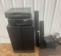 Receiver and CD changer stacked on floor speakers; slim satellite speakers, subwoofer, wire spool visible