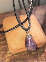 Necklace draped over display showing amethyst pendant and black braided cord