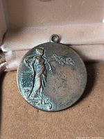 Front of bronze medal showing female figure, maple leaf shield and hanging loop