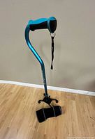 Full view of metallic teal quad cane showing ergonomic handle with wrist strap and knee brace placed at base