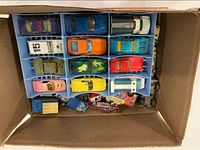 Top-down view of one tray inside cardboard box showing multiple diecast cars and some loose vehicles
