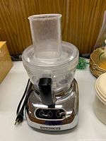 Front view of KitchenAid food processor showing chrome base, control buttons, clear work bowl and feed tube