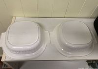 Two identical white plastic square dishes inverted showing external lids