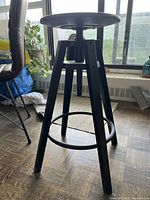 Full side view of black adjustable bar stool showing legs, footrest and height mechanism