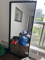 Full view of mirror leaning against wall showing black frame