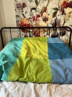 Full view of queen bed with colorful duvet; shows frame and mattress size
