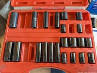 Red plastic case holding multiple black-oxide impact sockets, fractional sizes marked