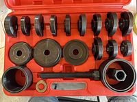 Open red plastic case showing steel driver discs, threaded forcing screw, collar and nut