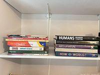 Two stacks of books on shelf showing spines: Humans, Battles That Changed History, ABC's of Nature, How in the World?, assorted cookbooks