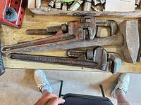overhead view showing three pipe wrenches stacked beside a sledge hammer