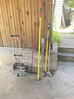 Entire lot leaning against wall: hand truck, poles, squeegee, scraper