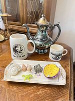 Group shot showing coffee pot, two mugs, tray with shells