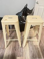 Front view of both cream metal bar stools showing overall design and finish