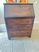 Front view of closed drop-front secretary desk showing three lower drawers, brass ring pulls and lock escutcheons