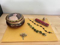 All items arranged on envelope: trinket box, Swiss Army knife, thimble, brooch, two bracelets