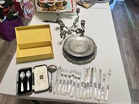 Full lot overview on table showing candelabrum, trays, cutlery, boxed spoons, ladle