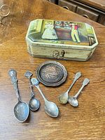 Group shot showing tin box, five spoons and Capilano plaque