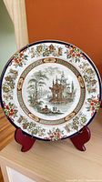 Full view of porcelain plate on stand showing entire scenic and border design