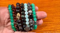 All eight gemstone stretch bracelets displayed on hand, showing bead colors and charms