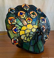 Front view of stained glass peacock lamp illuminated