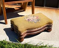 Walnut footstool angled view showing serpentine frame, bun feet and floral needlepoint top